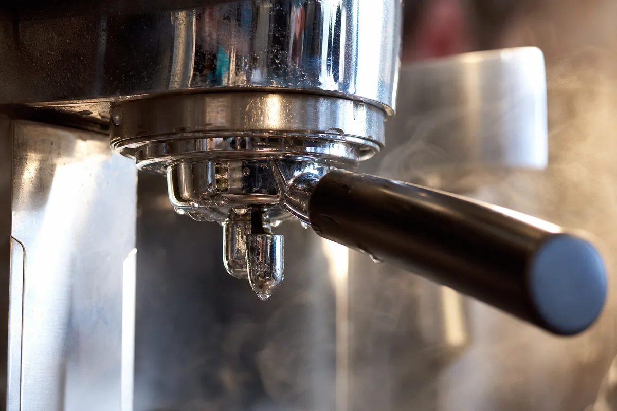 Détail du groupe en laiton chromé d’une machine à café de comptoir, porte-filtre verrouillé, vapeur en suspension