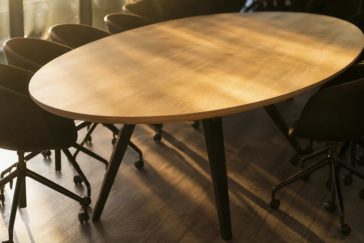 Salle de réunion vide d&rsquo;une PME française en fin de journée, chaises en bois autour d&rsquo;une table ovale nue, lumière dorée par de hautes fenêtres