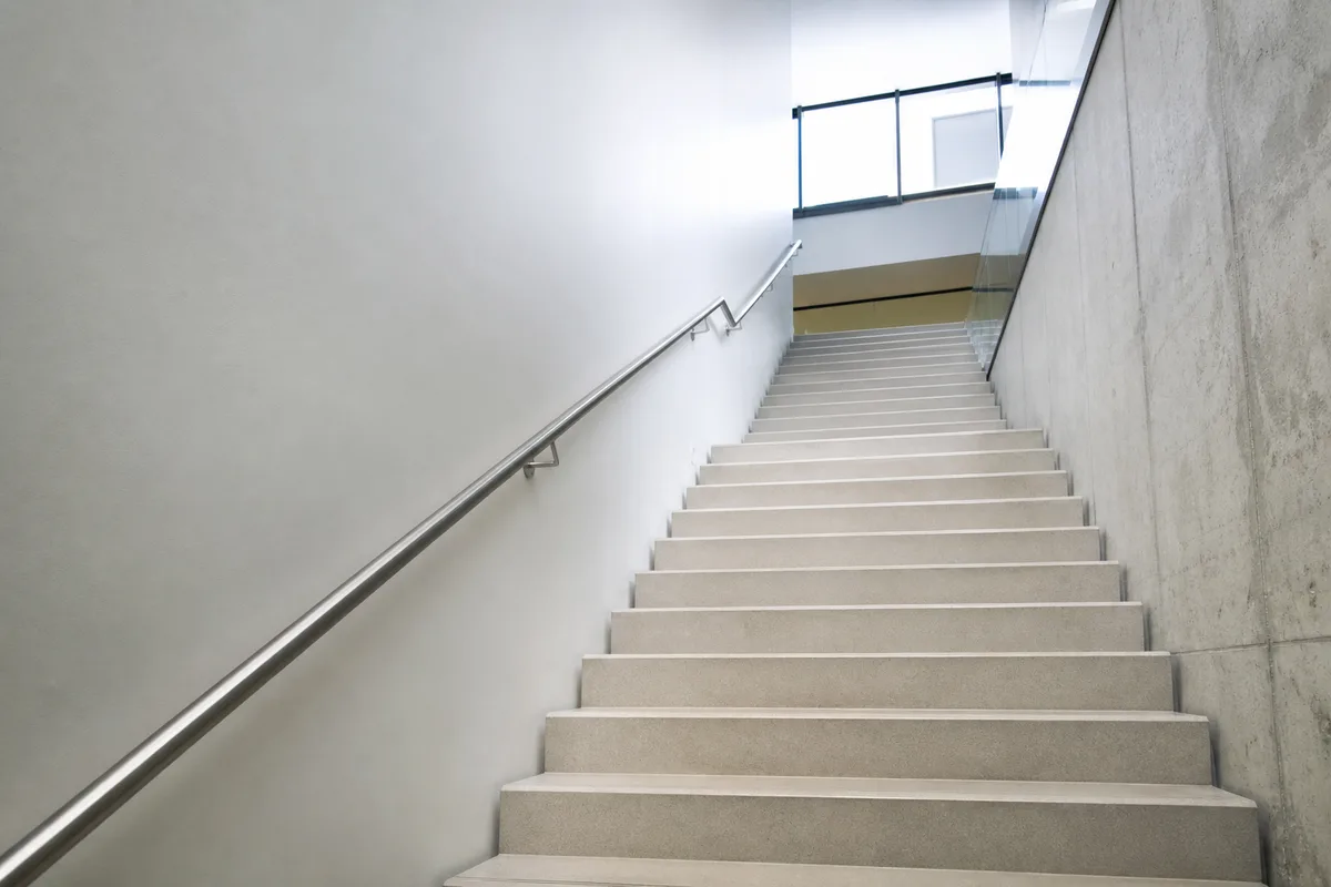 Escalier intérieur en béton clair avec main courante métallique, lumière naturelle venant d&rsquo;une baie en hauteur