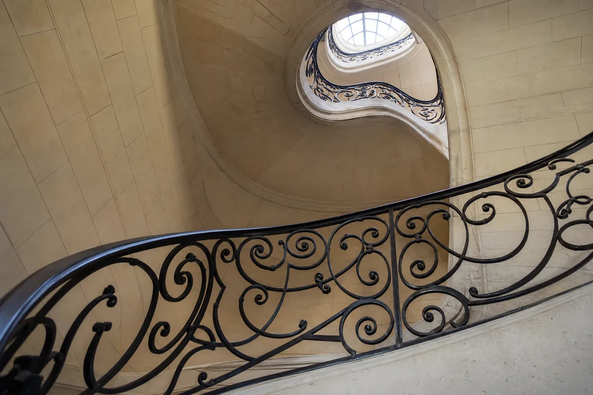 Escalier de pierre et rampe en fer forgé d&rsquo;un immeuble ancien baigné de lumière traversante
